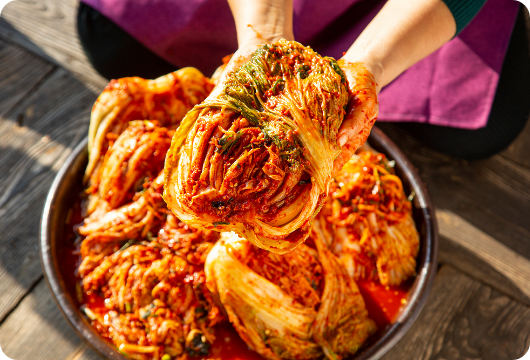 A picture of a bowl full of baechu kimchi and a person holding baechu kimchi